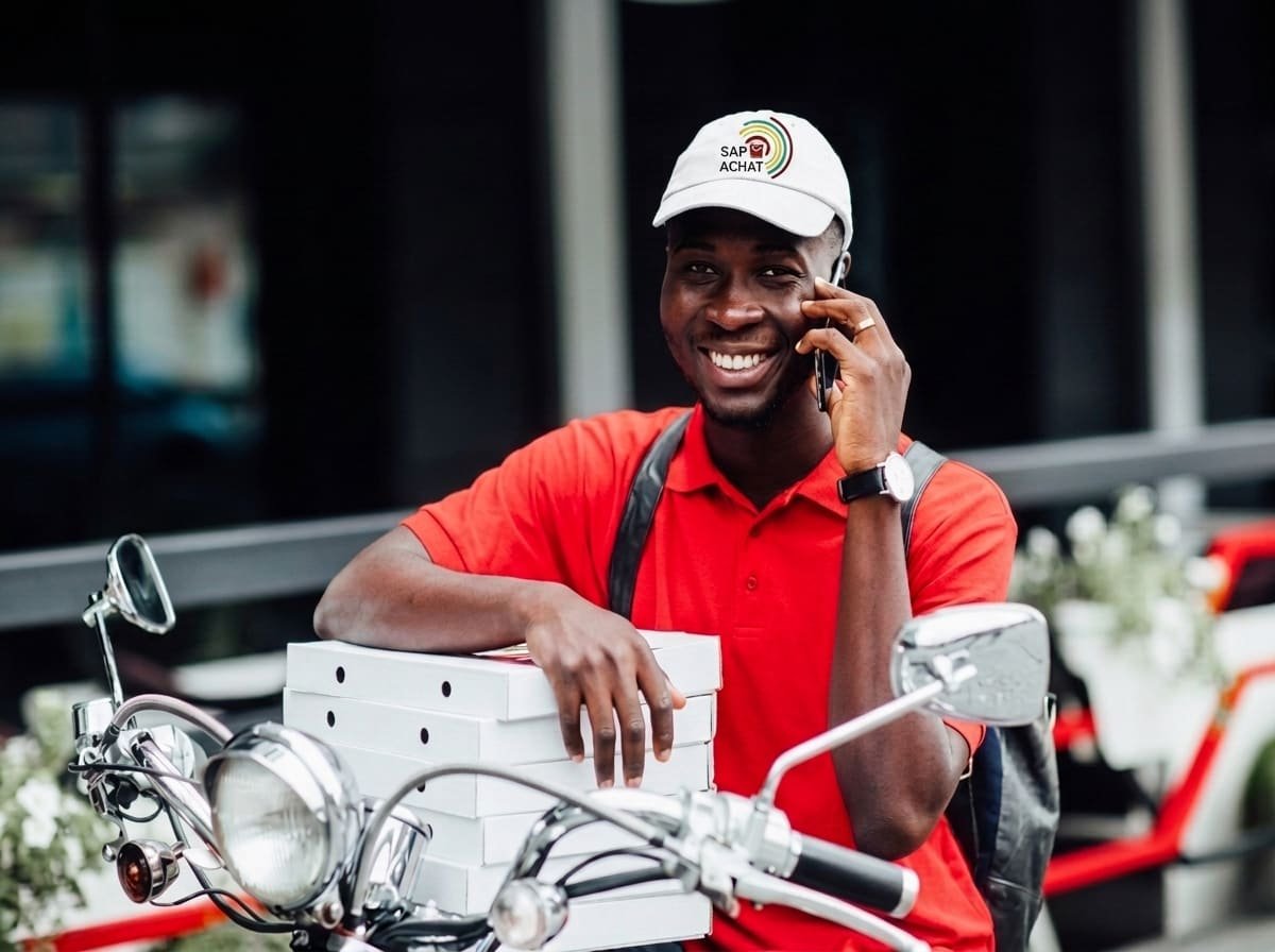 Livreur souriant au téléphone, colis chargés sur sa moto